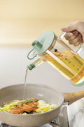 Glass cooking oil dispenser pouring oil into frying pan
