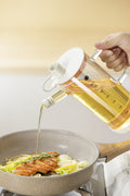 Glass cooking oil dispenser pouring oil into frying pan