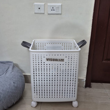 White laundry basket with 'VISUALIZE' branding on a tiled floor against a wall.