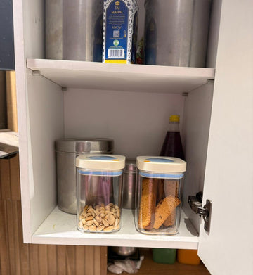 Open kitchen cabinet with food storage containers and bottles inside.