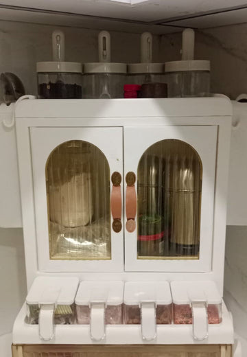 White kitchen storage unit with glass doors and a drawer, containing jars and containers.